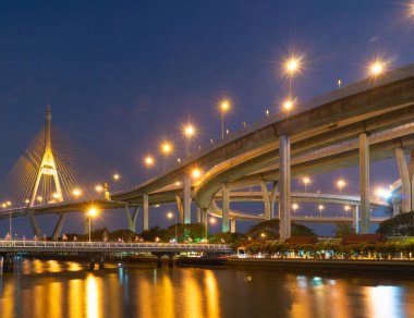 Gece aydınlanan modern köprünün çarpıcı görüntüsü aşağıdaki suya çok güzel yansıyor. Karmaşık tasarım ve canlı ışıklar büyüleyici şehir manzarası yaratır..