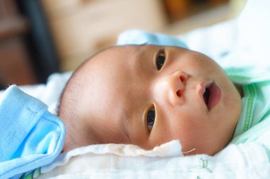 Yumuşak yüzeyde uzanan, açık yeşil elbiseli, mavi battaniyeli, meraklı ve masum bir bebeğin yakın çekimi.