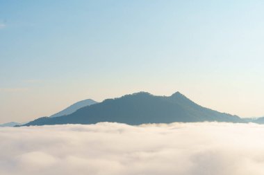 Berrak mavi gökyüzünün altında bulutlar denizinden yükselen sakin bir manzara huzur ve huzur hissi uyandırıyor.