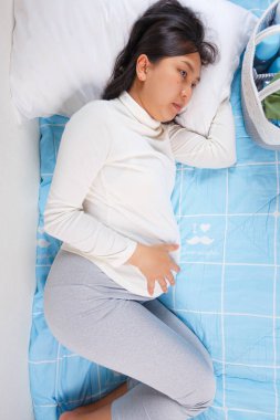 Mavi yatak örtüsüne uzanmış elini karnına koyup dalgın dalgın yatan bir kadın. Sahne, sakinlik ve içgözlem duygusunu ifade eder.