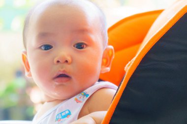 Meraklı, geniş gözlü bir bebek turuncu bebek arabasında oturuyor ve etraflarındaki dünyayı keşfediyor. Yumuşak ışık masum ifadelerini ve neşeli kıyafetlerini vurgular