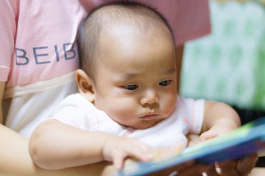 Yetişkinler tarafından tutulan, merakını ve nişanını belli eden odaklanmış bir bebek kitabı. yumuşak ışıklandırma çocuk ifadesini ve anın sıcaklığını vurgular