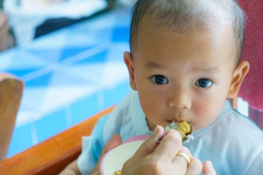 Meraklı bakışları ve neşeli ifadesiyle yemeğin tadını çıkaran bir çocuk.