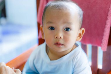 Tahta sandalyede oturan, etrafa bakan, büyük gözlü meraklı bir bebek.