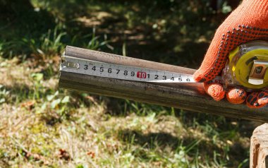 İki demir boru ve uzunluğunu ölçen bir mezura ile eldivenli bir el.