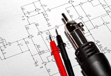 Kırmızı ve siyah sondalar ve elektronik devre diyagramının arka planında lehim saç kurutma makinesi var.
