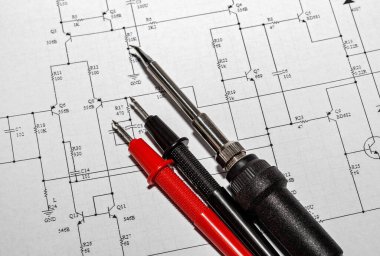 Elektronik devre diyagramının arka planına karşı kırmızı ve siyah sondalar ve lehimleme demiri