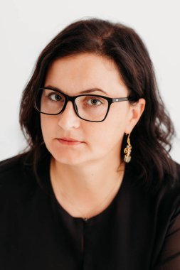 40 yaşında, kendine güvenen, zarif siyah bir elbise ve temiz beyaz bir arka planda gözlük takan bir kadının stüdyo portresi. Profesyonellik ve entelektüellik sergiliyor, imajı iş, şirket, moda ve yaşam tarzı için ideal kılıyor.