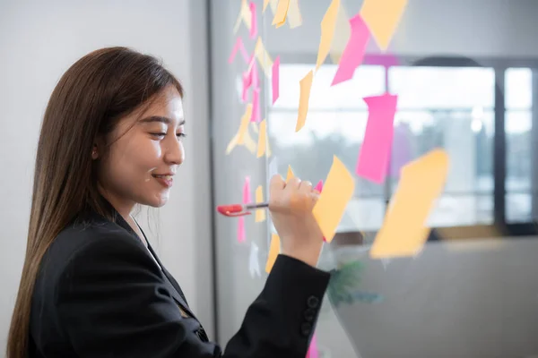 Business woman use post it notes to share idea. Sticky note on glass wall