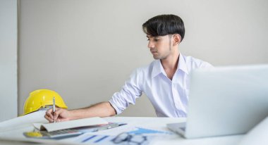 İşadamı bilgisayarla çalışıyor ve masasında belgeler var. Ofisteki verileri analiz ediyor.