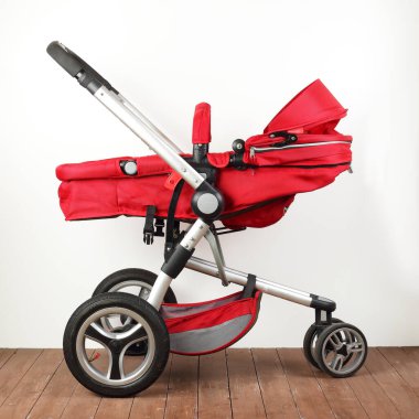 Beyaz bir duvar ve ahşap zemin üzerinde kırmızı evrensel bebek arabası