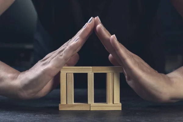 木製のキューブハウスに彼女の手で屋根を作る女性は彼女の財産と投資を保護します 木造住宅暗い背景 — ストック写真