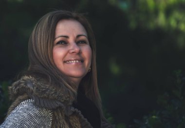 Doğada gülümseyen orta yaşlı sarışın kadın portresi. Odaklanamayan koyu yeşil arka plan. Yaşam tarzı kavramı.