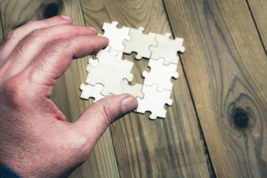 Bir el kayıp bir yapboz parçasını tutuyor. Yapboz dört parçalı bir kare. Sahne, kişinin bulmacayı tamamlamaya çalıştığı gibi hüsran ve kararlılığın bir parçasıdır.