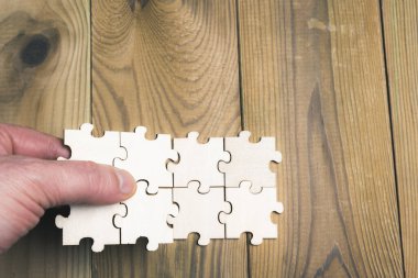 Tahta bir masanın üzerindeki yapboz parçalarını birleştiren insan eli. İş kavramı, sendika ve iş büyümesi.