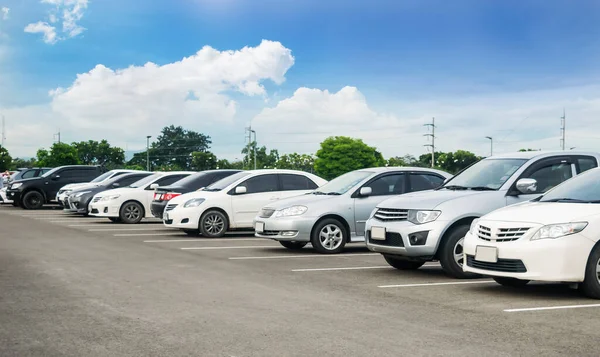 Car parking in large asphalt parking lot with trees, white cloud and blue sky background. Outdoor parking lot with fresh ozone and green environment of transportation concep