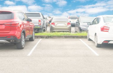Asfalt otoparkta araba parkı ve beyaz bulutlu ve mavi gökyüzü arka planlı boş bir park yeri. Açık hava otoparkı. Taze doğa ve yeşil ulaşım ve teknoloji ortamı.