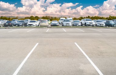 Geniş, boş asfalt park alanı arka planı. Arka planda bir sürü araba var. Ağaçları ve bulutlu gökyüzü olan boş bir park yeri. Park yerinin dışında.
