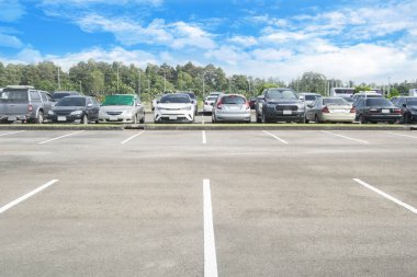 Geniş, boş asfalt park alanı arka planı. Arka planda bir sürü araba var. Ağaçları ve bulutlu gökyüzü olan boş bir park yeri. Park yerinin dışında.