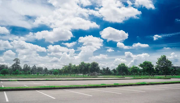 Wide empty asphalt parking lot background with white painted lines marked lens. Outdoor empty space parking lot with trees and cloudy sky. outside parking lot in a par