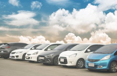 Depoda arka arkaya arabaları park ediyor. Araç nakliyesi envanter malları. Beyaz bulutlu ve mavi gökyüzü arka planlı büyük bir asfalt otoparka park edilmiş bir araba. Açık hava parkı lo