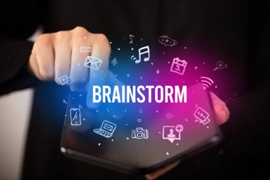 BREINSTORM yazıtlı, sosyal medya kavramına sahip katlanabilir bir akıllı telefon tutan bir iş adamı