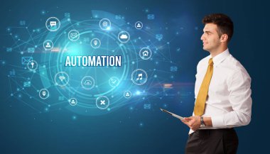 Teknolojiyle ilgili ikonlar ve AUTOMATION yazıtları ve modern teknoloji kavramı önünde düşünen iş adamı.