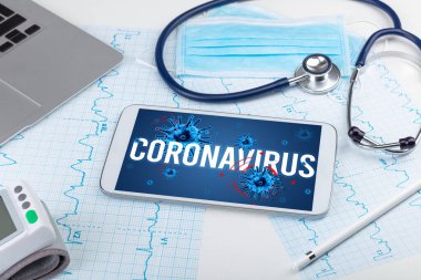 Beyaz yüzeyde CORONAVIRUS yazıtı, salgın konsepti içeren tablet pc ve doktor araçları