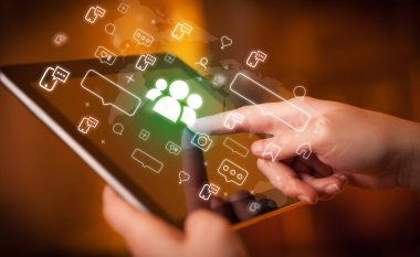 İçinden insan simgeleri çıkan tablet kullanan bir elin yakın çekimi, sosyal medya kavramı