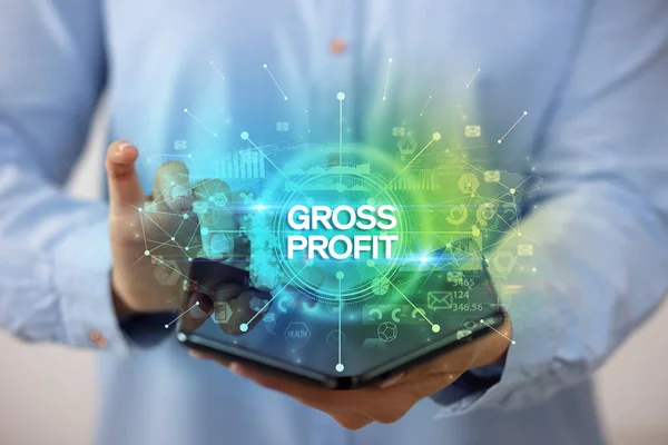 ビジネスマンは Gross Profitの碑文 新しいビジネスコンセプトを持つ折り畳み式のスマートフォンを保持 — ストック写真