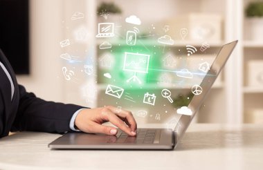 Dizüstü bilgisayarda çalışan iş adamı, içinden resim çizelgeleri çıkıyor, iş dünyası kavramı büyüyor.