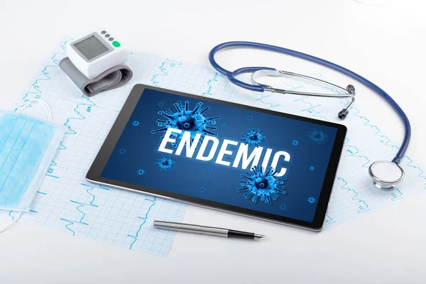 Tablet pc and doctor tools on white surface with ENDEMIC inscription, pandemic concept