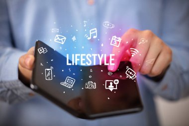 İş adamı, üzerinde LIFESTYLE yazıları ve sosyal medya kavramı olan katlanabilir bir akıllı telefon tutuyor.