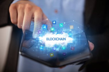 Blockchain yazıtlı, teknoloji konseptli katlanabilir bir akıllı telefon tutan bir iş adamı.