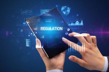 İş adamı katlanabilir bir akıllı telefon tutuyor. Üzerinde REGULAON yazıtları var. Başarılı bir iş konsepti.