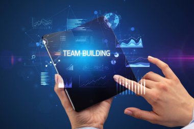 İş adamı takım oluşturma yazıtları ve başarılı iş konsepti içeren katlanabilir bir akıllı telefon tutuyor.