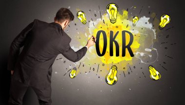 İş adamı OKR kısaltması ile renkli ampul çiziyor, yeni teknoloji fikri kavramı