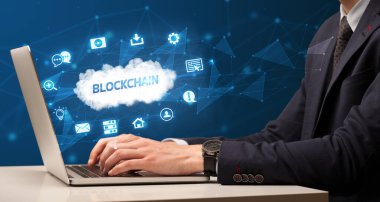 Blockchain yazıtları ve modern teknoloji konseptiyle dizüstü bilgisayarda çalışan bir iş adamı.