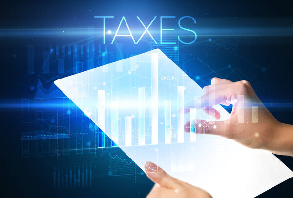 Рука держит футуристический планшет с надписью TAXES выше, современная бизнес-концепция