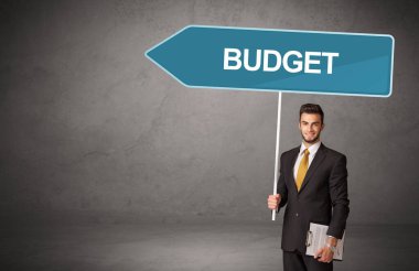 Bütçe yazıtları ve yeni iş yönü konseptiyle günlük bekleme yolu tabelasında genç iş adamı