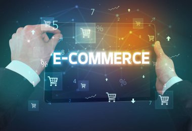 E-COMERCE yazıtları ve online alışveriş konseptiyle el ele tutuşan tabletin yakın çekimi