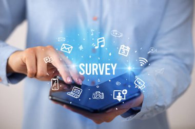 İş adamı elinde katlanabilir bir akıllı telefon tutuyor. Üzerinde SURVEY yazıları, sosyal medya kavramı var.
