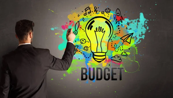 Businessman Drawing Colorful Light Bulb Budget Inscription Textured Concrete Wall — Stock Photo, Image