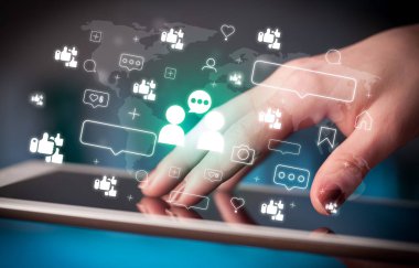 Tablet kullanan ve içinden ikonlar çıkan bir elin yakın plan resmi, sosyal medya kavramı