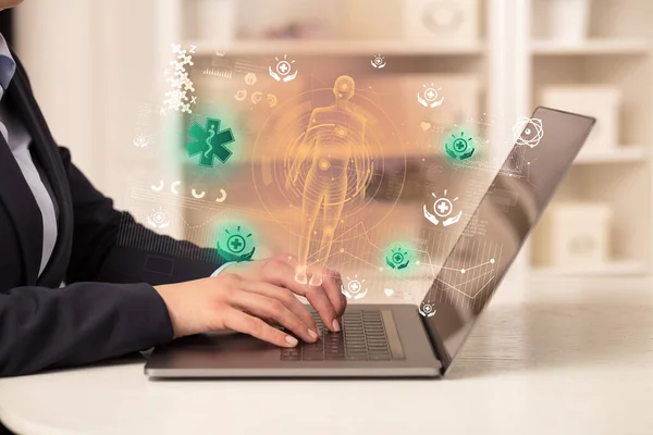 Doctor working on laptop with pharmacy icons coming out from it, healthcare concept