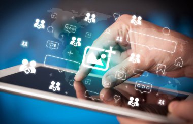 Tablet kullanan ve içinden fotoğraf simgeleri çıkan bir elin yakın plan görüntüsü, sosyal medya kavramı