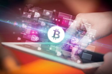 İçinden bitcoin simgeleri çıkan tablet kullanan bir elin yakın çekimi, dijital para birimi kavramı