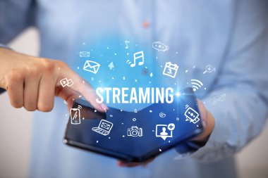 İş adamı elinde katlanabilir bir akıllı telefon tutuyor. Üzerinde STREAMING yazıtları ve sosyal medya kavramı var.