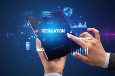 İş adamı katlanabilir bir akıllı telefon tutuyor. Üzerinde REGULAON yazıtları var. Başarılı bir iş konsepti.