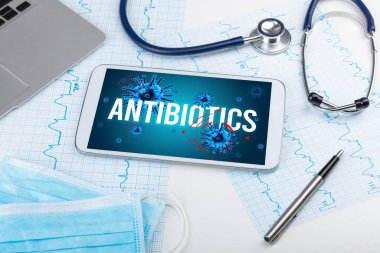 Beyaz yüzeyde ANTIBIOTICS yazıtları, salgın konsepti olan tablet pc ve doktor araçları